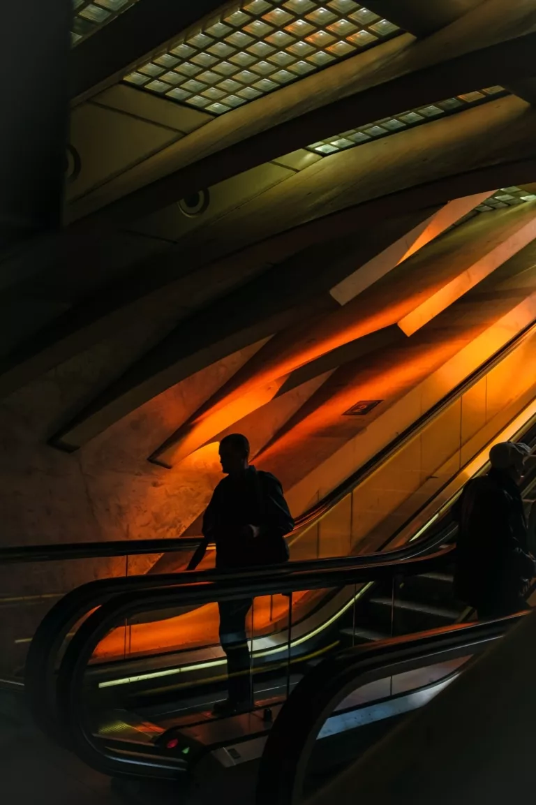 Silhouette sur l’escalator éclairé en orange à la gare de Liège-Guillemins