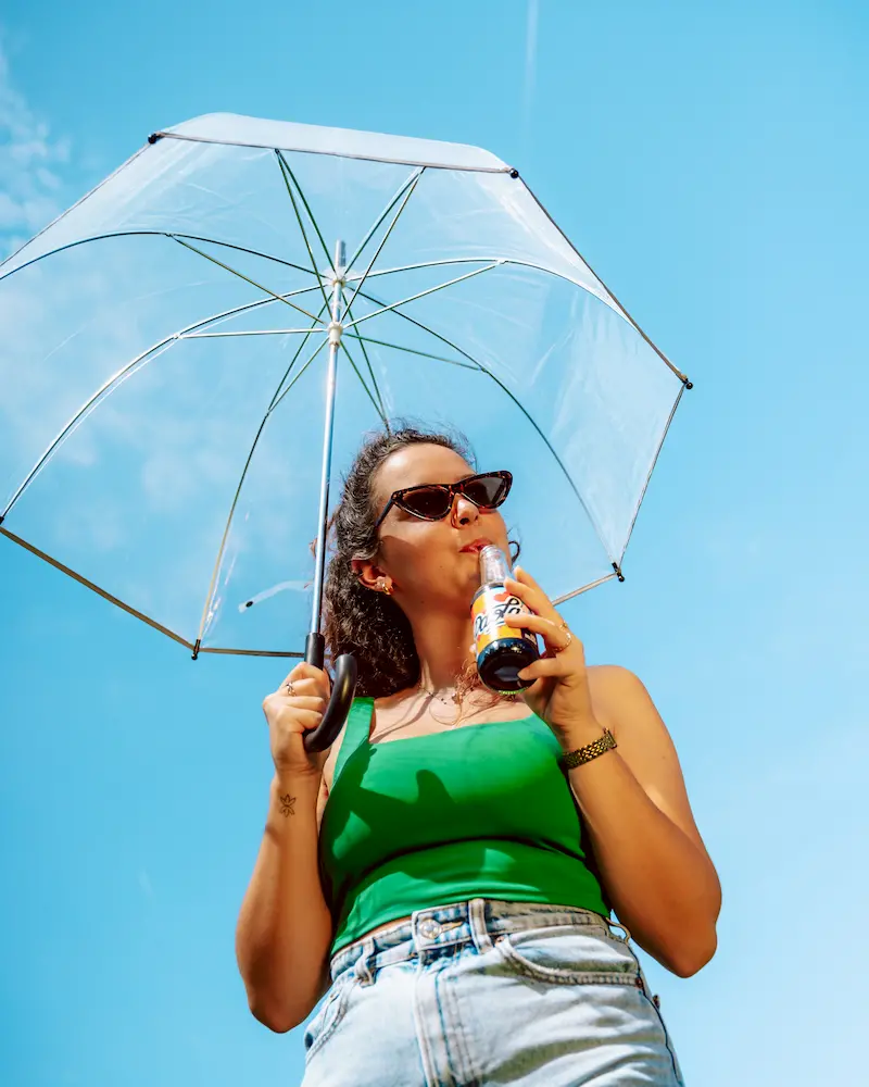 Jeune femme au parapluie transparent qui boit un Paola Cola