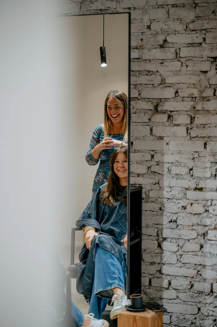 Coiffeuse et cliente qui sourient dans le miroir à l’Atelier Victoria